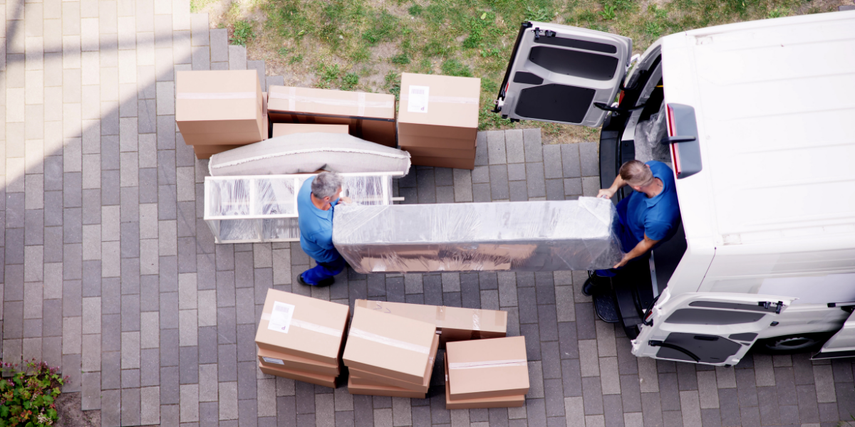 two delivery men removing bulk furniture items from a white van and on to a driveway