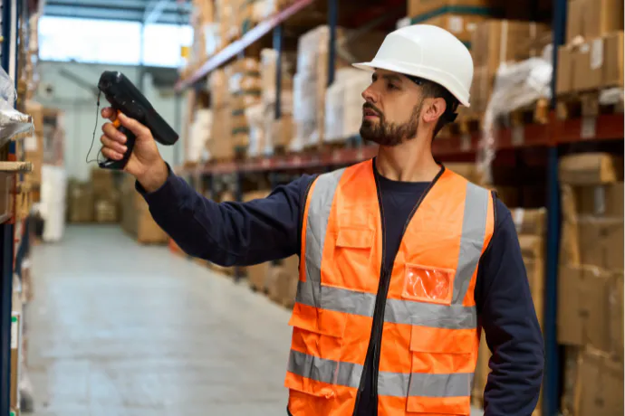 Man in hi-vis vest with hard hat, using a hand-held scanner to scan stock in a warehouse