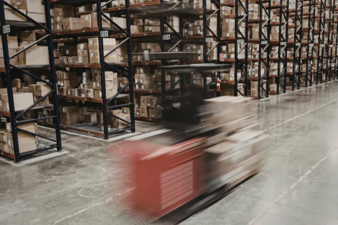 boxes stored in a warehouse on black metal shelving with a fork lift passing in front